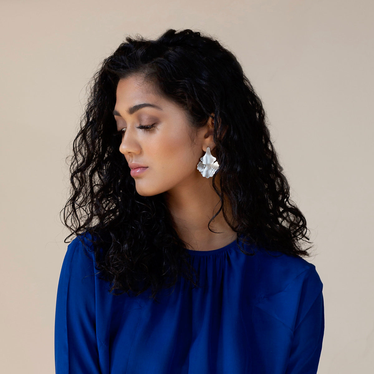 Woman with head tilted thoughtfully while wearing plume large fan silver earrings